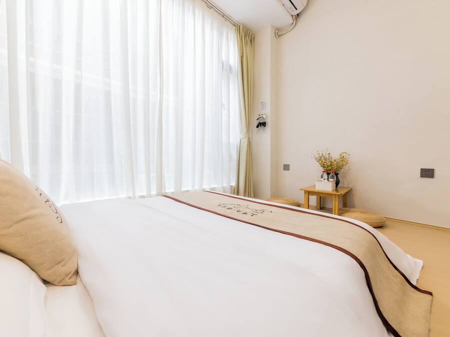 Habitación de hotel con una cama grande, una mesita de madera con un florero y cortinas de gasa.