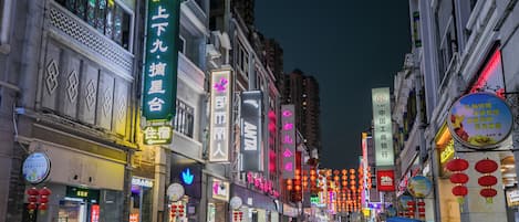 Una animada calle urbana nocturna con señalización iluminada y faroles tradicionales.