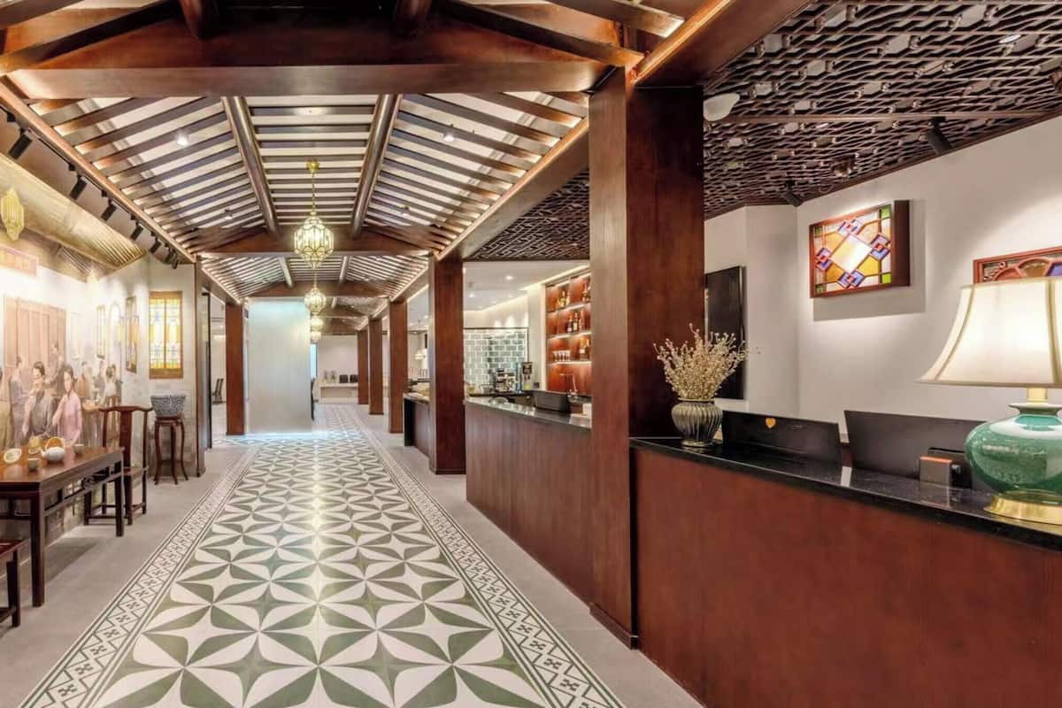 Um hall de hotel com um corredor comprido, mobiliário de madeira, piso estampado e um balcão de recepção.