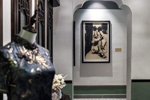 Una fotografía en blanco y negro en un marco colgada en una pared, un jarrón decorativo con flores, y una zona con azulejos verdes.