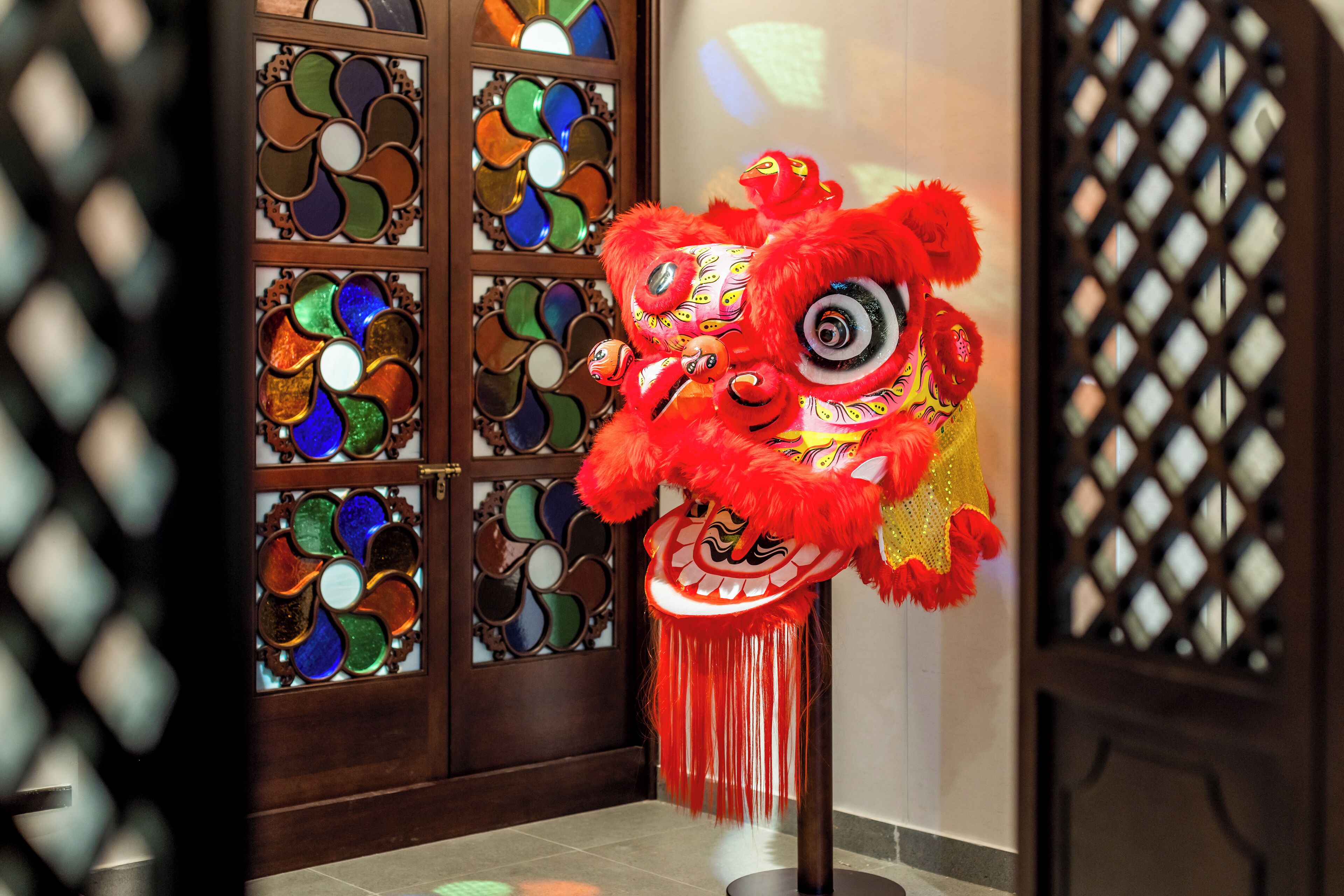 Un traje de danza del león rojo en una habitación con puerta de madera y ventanal con vidrieras de colores.