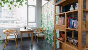 Een kamer met een houten bureau, twee stoelen, een boekenkast en uitzicht op gebouwen door een raam.
