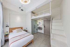 A modern bedroom with a large bed, a built-in desk, a vanity with a mirror, and a staircase leading to an upper level.