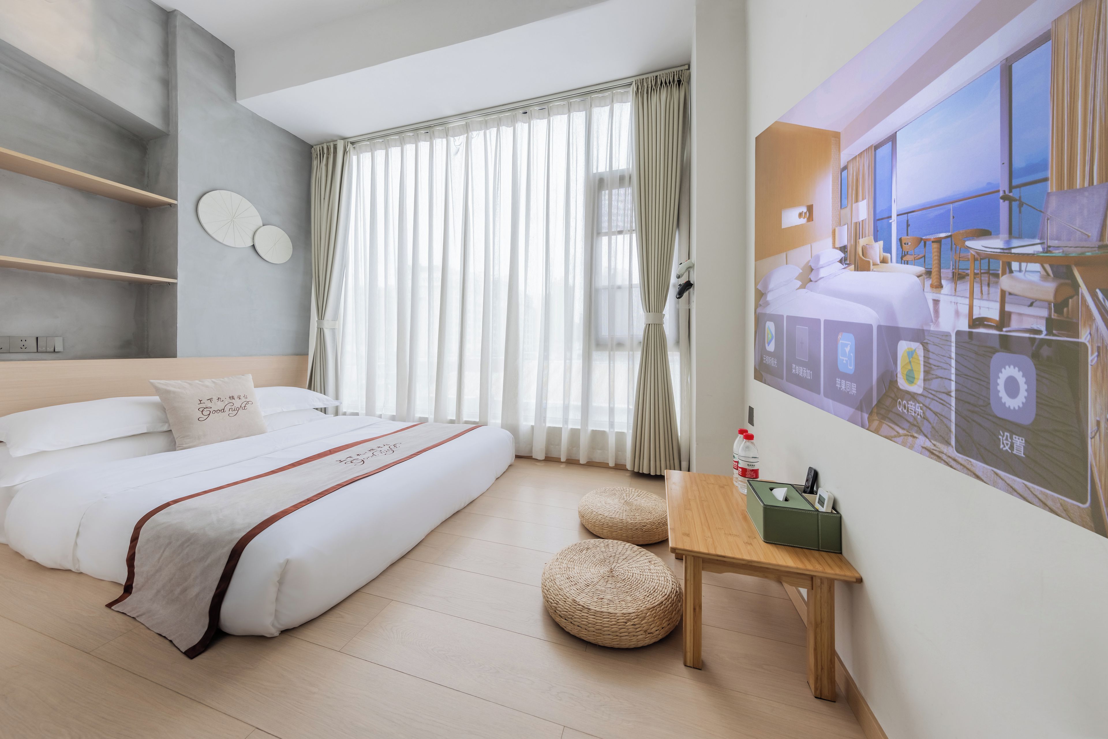 A modern hotel room with a large bed, a wooden table, and a view of the sea through large windows.