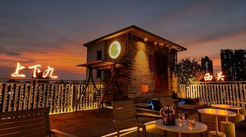 Un bar sul tetto con posti a sedere all'aperto, un piccolo edificio con insegna al neon e uno skyline cittadino sullo sfondo.