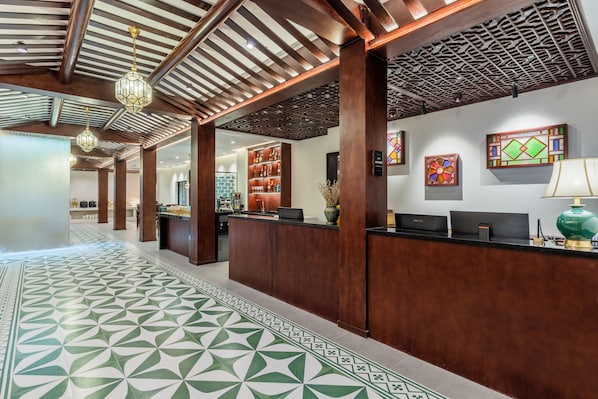 A reception area with a patterned floor, wooden reception desk, and a wall with a decorative glass piece. - Stargazing Platform Inn - Heart of Old Canton (Guangzhou)