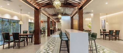 A spacious hotel lobby with a central bar, multiple seating areas, and a patterned floor.