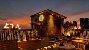 A rooftop bar with a small stone building, outdoor seating, and illuminated signage.