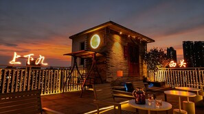 A rooftop bar with a small stone building, outdoor seating, and illuminated signage. - Stargazing Platform Inn - Heart of Old Canton (Guangzhou)