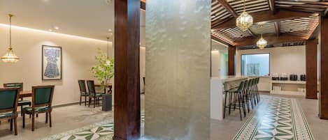 A modern hotel lobby with a patterned floor, wooden pillars, a bar area, and a dining setup.