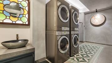 A laundry room with a large wall-mounted washing machine and dryer, a bowl sink, and a decorative stained glass window.