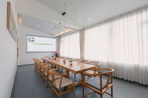 Un salón de conferencias con una larga mesa, sillas, una pantalla de proyector y un amplio ventanal con cortinas.