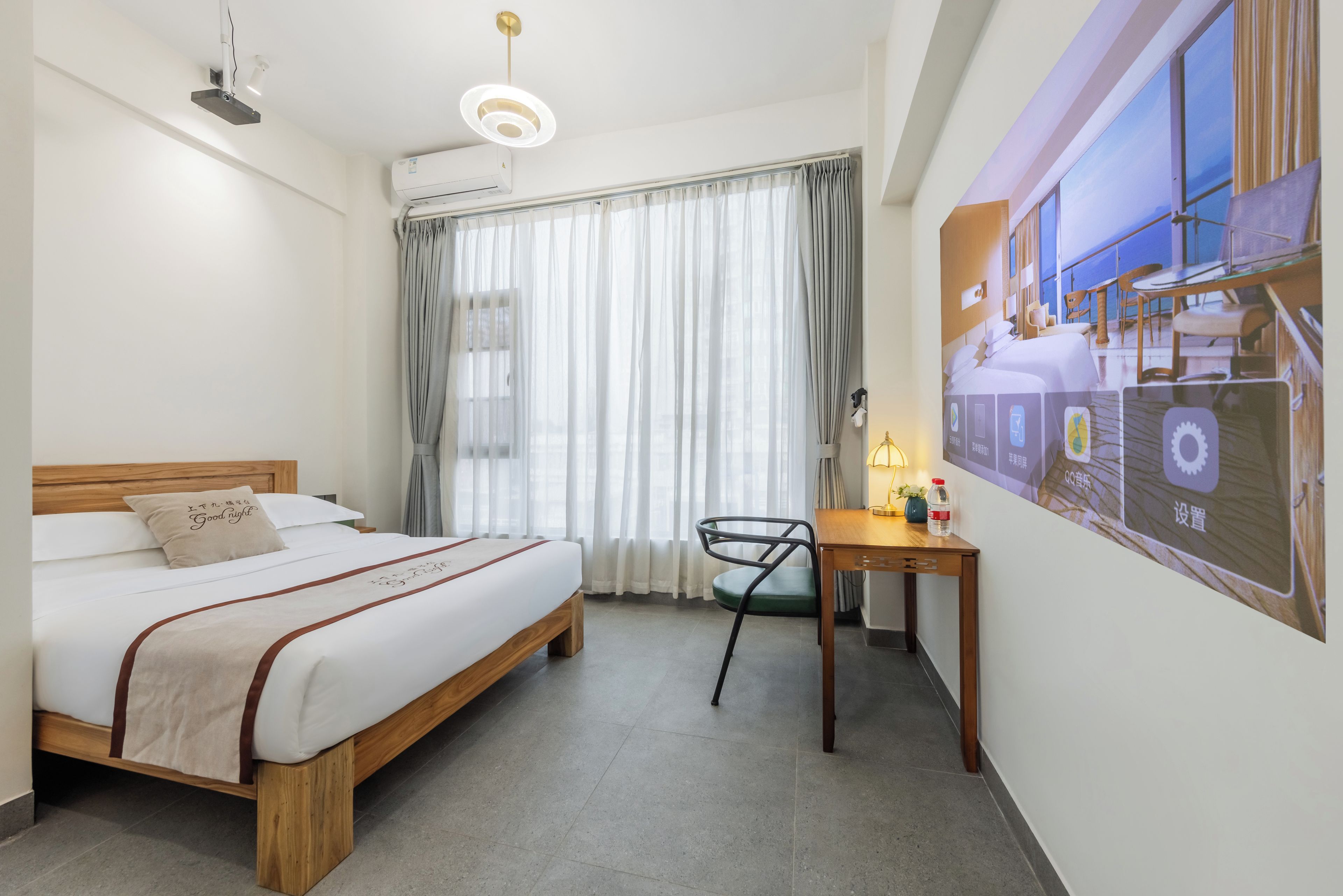 Une chambre d’hôtel équipée d’un lit, d’un bureau, d’une chaise, d’une fenêtre avec des rideaux, d’un climatiseur et d’un panneau de commande fixé au mur.