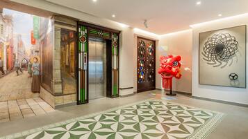 Un vestíbulo de hotel con un ascensor tradicional, una figura de león danzante rojo y una obra de arte moderno.
