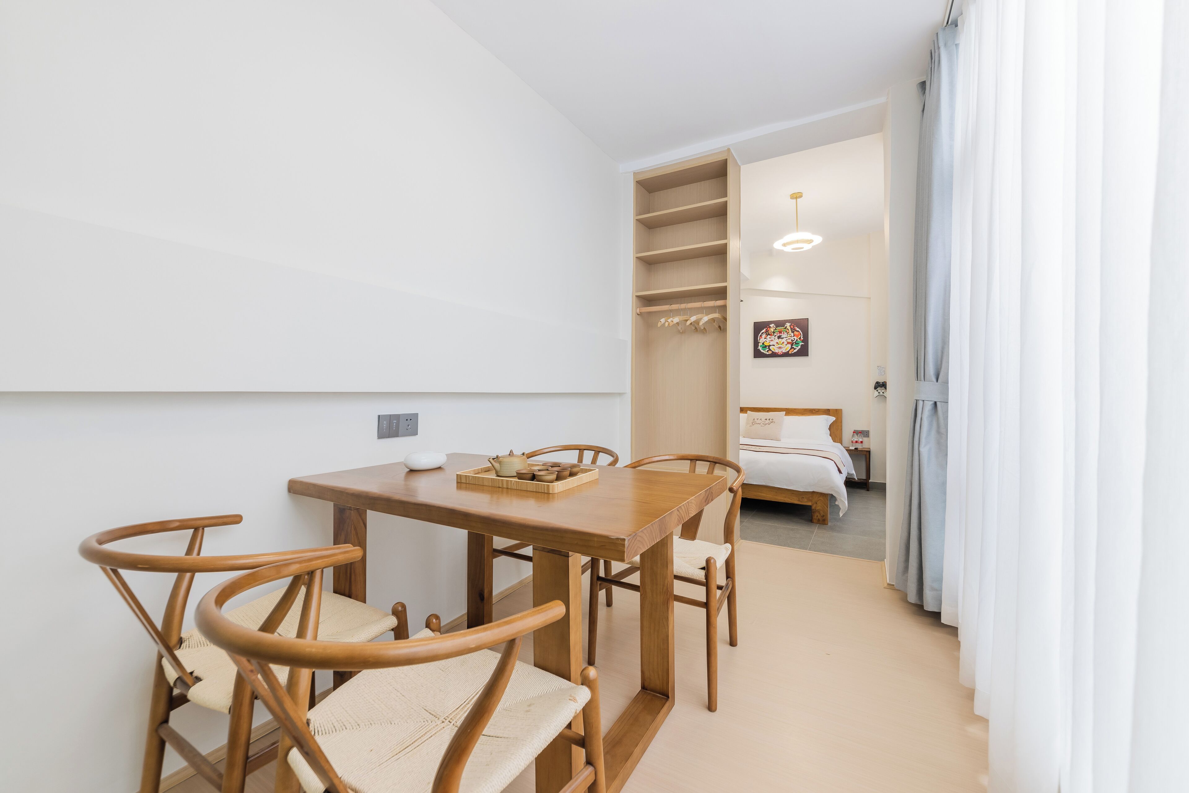 Una habitación moderna con una mesa de comedor de madera y sillas, una cama con edredón blanco y un armario con espacio para colgar.
