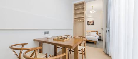 Una habitación moderna con una mesa de comedor de madera y sillas, una cama con edredón blanco y un armario con espacio para colgar.