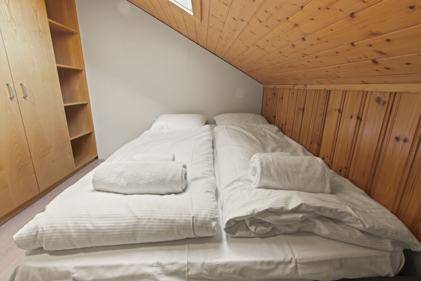 A bedroom with a wooden ceiling, two beds with white linens, and a wooden wardrobe.