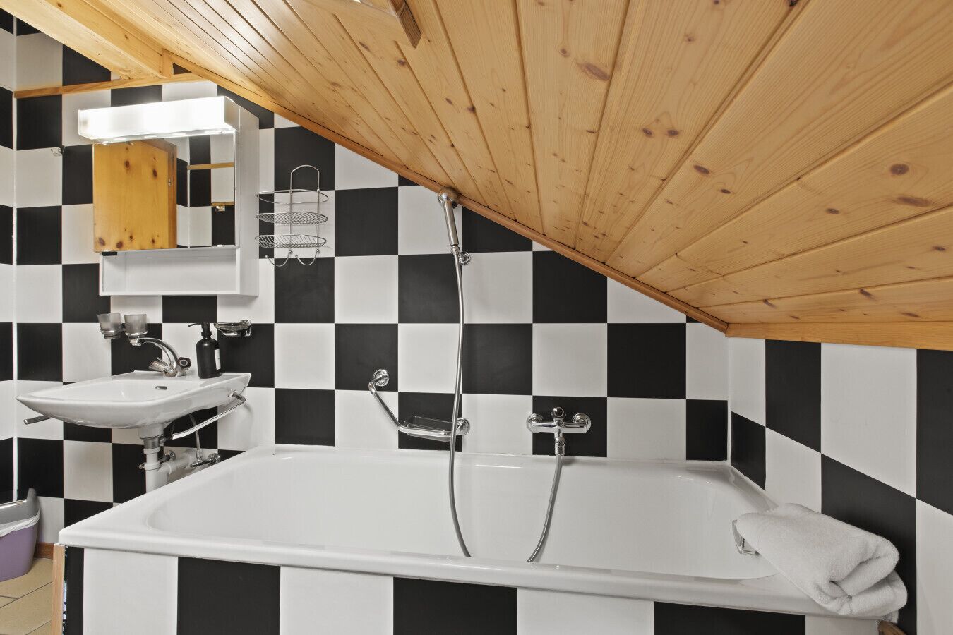 A bathroom with a checkered black and white tile wall, a wooden ceiling, a white bathtub, and a sink with a mirror above it.
