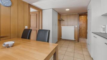 A compact kitchen with a wooden table, chairs, a clock, and white cabinets.