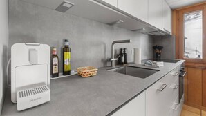 Une cuisine moderne avec un plan de travail gris, un évier encastré, une machine à café et un panier de citrons.