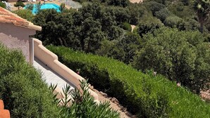 Paisaje costero con piscina, abundante vegetación y colinas al fondo.