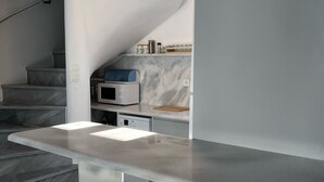 A modern kitchen with a marble countertop, a built-in oven, and a microwave. There is a staircase with a marble finish leading to another level.