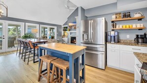 A modern kitchen with a central island, stainless steel appliances, and a view through large windows.