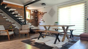En moderne stue med trappe, møbler i træ og et stort vindue med skodder.