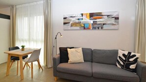 Un salon moderne avec un canapé gris, une table à manger avec des chaises et un grand tableau abstrait accroché au mur.