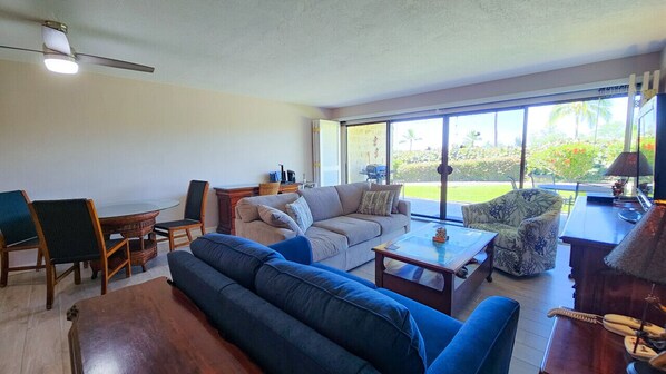 A spacious living room with a large window, a ceiling fan, and a dining area with a table and chairs.