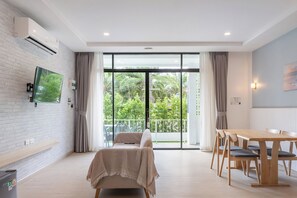Una habitación moderna con una cama, una mesa de comedor con sillas, un televisor montado en una pared de ladrillo y un balcón con vistas al verdor.