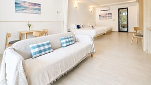 Ein modernes Hotelzimmer mit einer Couch, zwei Betten, einem Essbereich und Blick aufs Meer.