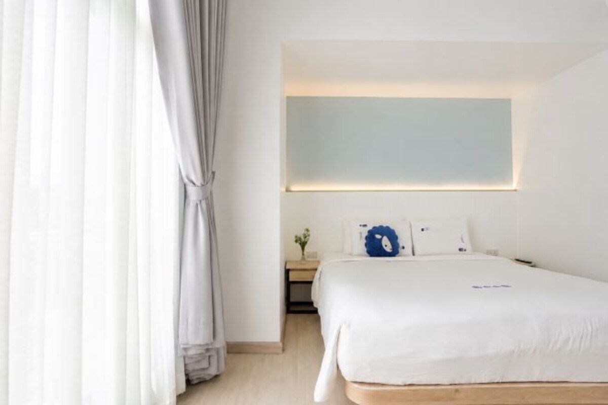 Una habitación de hotel con cama, mesita de noche y lámpara de pared.