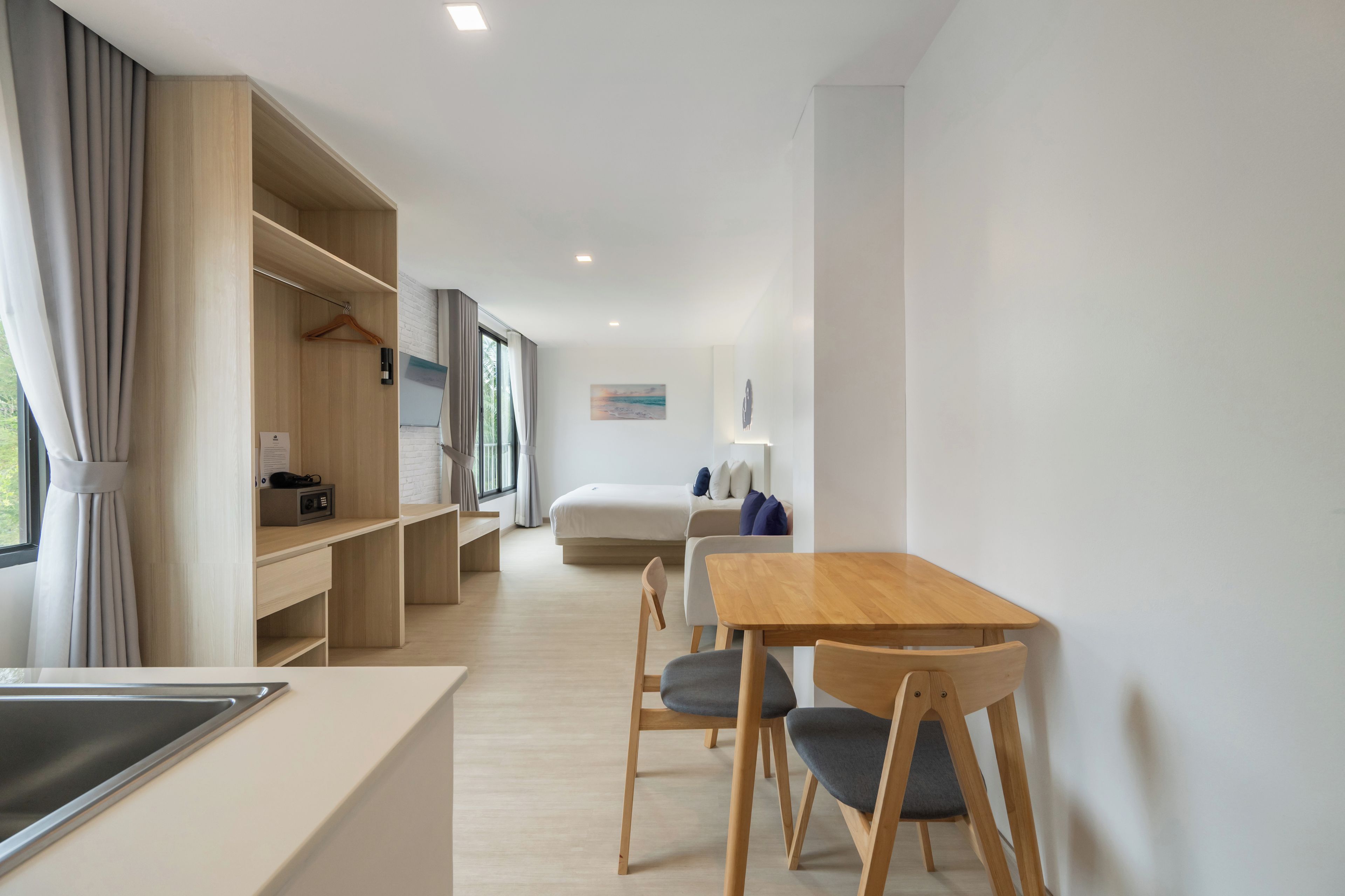 A modern hotel room with a wooden desk, chairs, a bed, and a wardrobe.