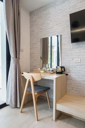 Habitación moderna con escritorio de madera, una silla, televisor de pantalla plana montado en una pared de ladrillo y una ventana con cortinas.