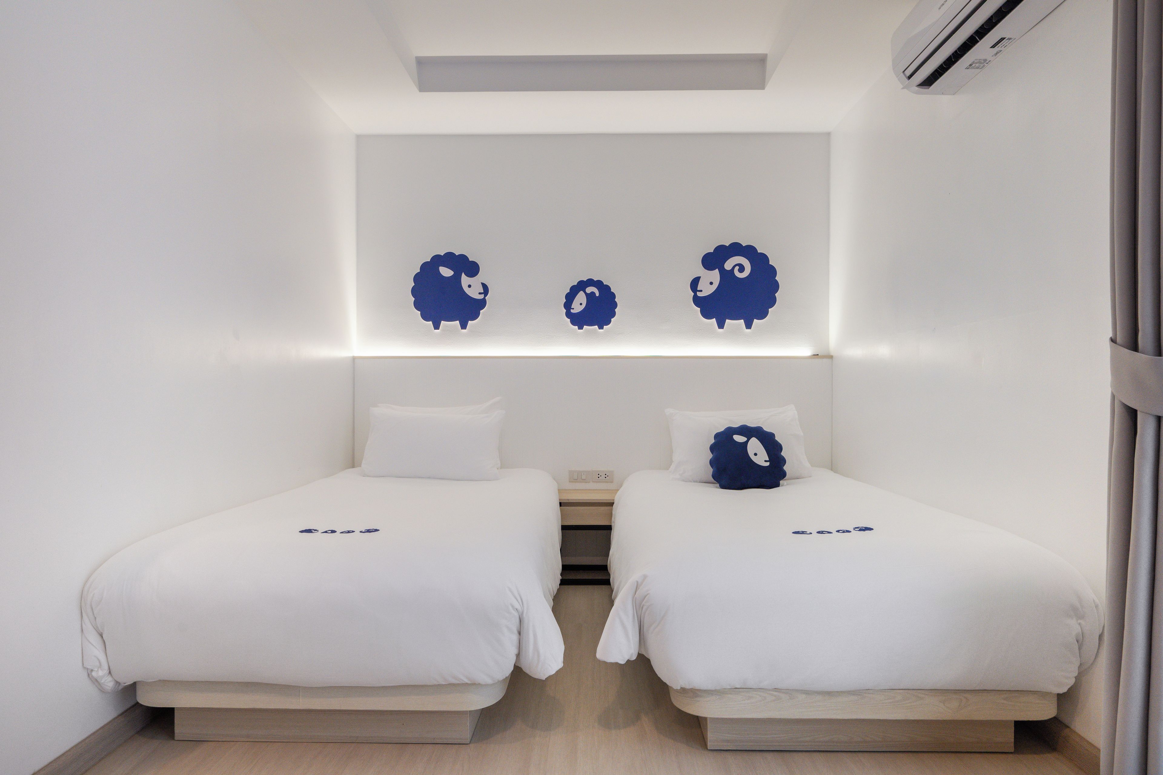 A hotel room with two beds, a wall-mounted air conditioner, and a ceiling light fixture.