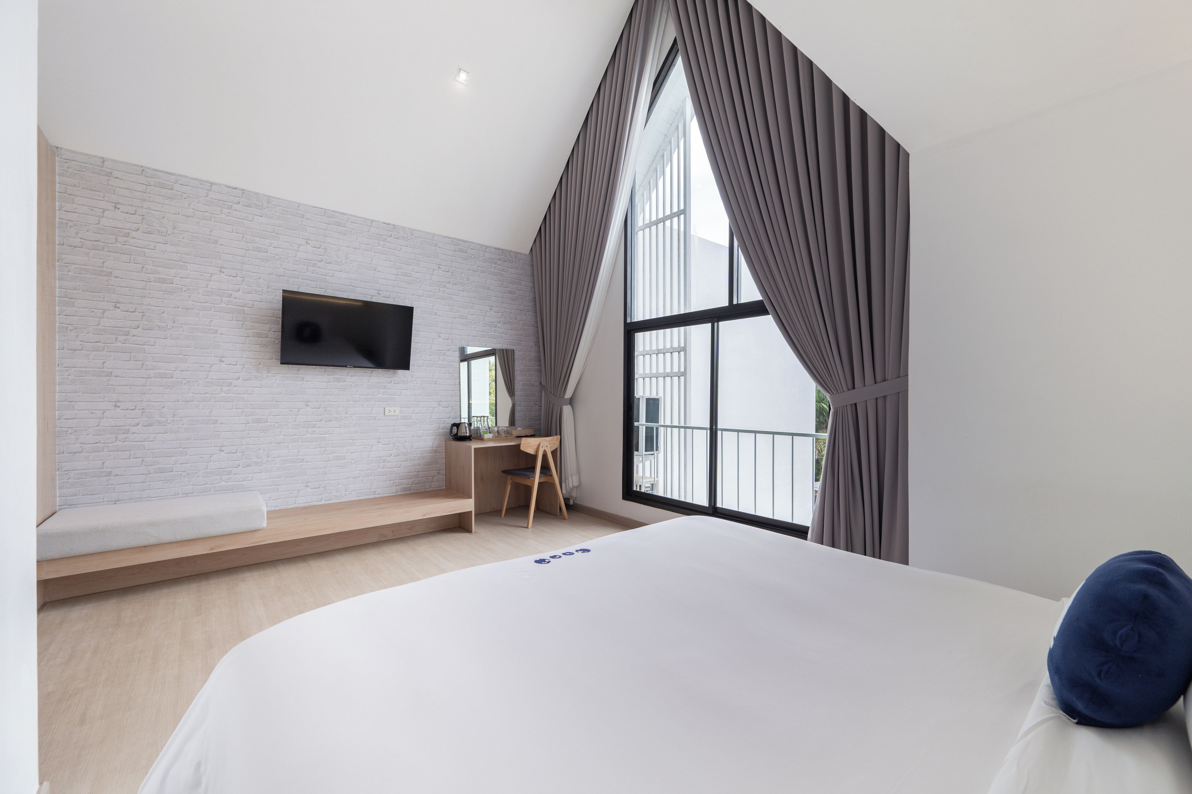 A modern bedroom with a large bed, a desk, and a TV mounted on a brick wall.