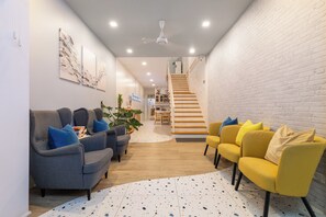 Una sala moderna con sofás grises y amarillos, una pared de ladrillo blanco y una escalera que sube a otro nivel.