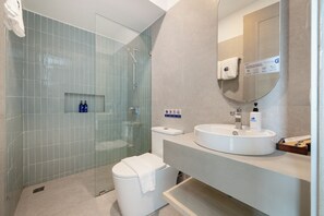 Un baño moderno con ducha envuelta en cristal, inodoro blanco y lavamanos con espejo.