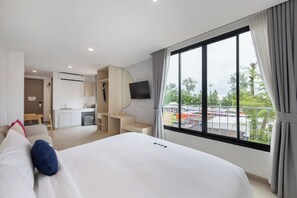 Habitación de hotel con cama, escritorio, televisor y balcón con vistas.