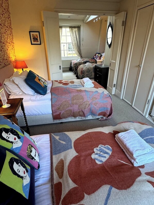 A hotel room with two beds, a nightstand, a lamp, a mirror, and a door leading to another room.