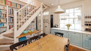 A dining area with a wooden table, chairs, a staircase, and bookshelves filled with books. - Luxury Cottage in the Heart of Bath (Bath)
