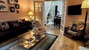 A living room with a glass coffee table, a sofa, a patterned armchair, and a TV mounted on the wall. - Luxury Cottage in the Heart of Bath (Bath)