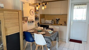 A compact kitchen with modern appliances, a dining area with striped tablecloths, and a wooden cabinet with glass doors. - CALLEA II - Holiday home with garden in Carnac - K16 (Carnac)