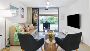 Uma sala de estar moderna com um sofá, duas poltronas, uma TV e uma varanda com mobiliário de exterior.