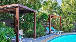 Uma área à beira da piscina com pergolado, espreguiçadeiras e piscina.