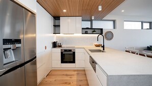 Una cocina moderna con electrodomésticos de acero inoxidable, armarios blancos y techo de madera.