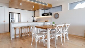 Una cocina moderna con armarios blancos, una mesa de comedor de madera con sillas blancas y un ventanal grande.