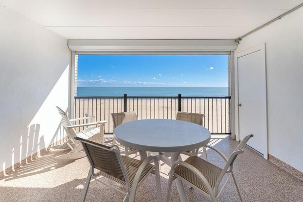 Un balcon avec une table ronde et des chaises, une vue sur la mer et une porte blanche.