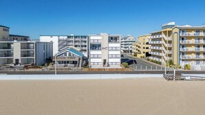 A beachfront hotel with multiple floors, a swimming pool, and a beach in the foreground. - Oceanfront Three Bedroom Condo on the Boardwalk (Ocean City)
